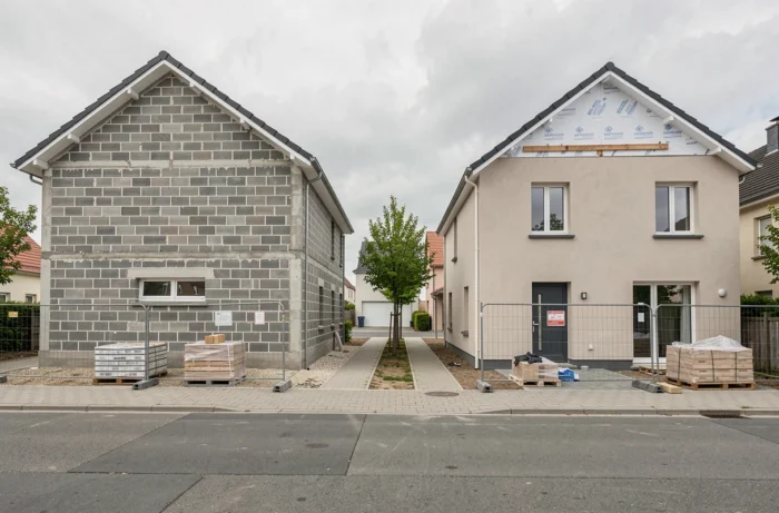 Deux maisons en construction côte à côte, l'une en parpaing et l'autre avec isolation en polystyrène, dans un quartier résidentiel